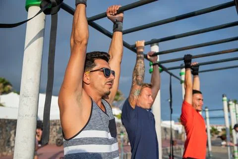 Three men train by doing pull ups in an open air gym, sport and healthy lif.. Stock Photos