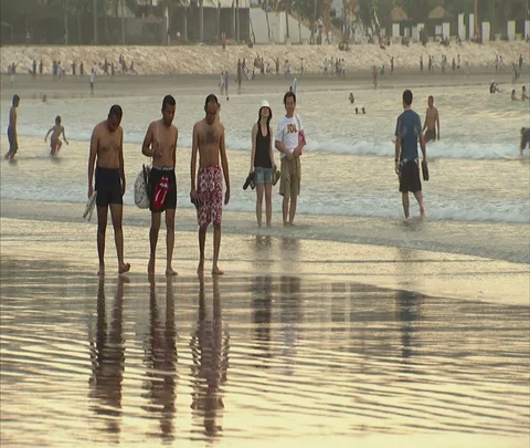 Three men walking across beach at water's edge Stock Footage 86747262