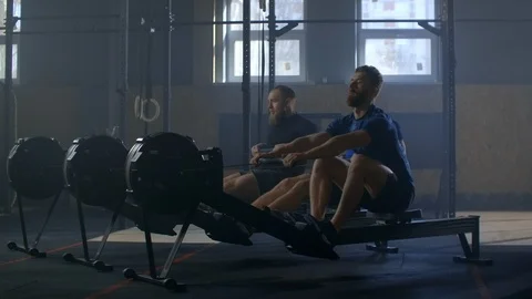 Three men work out together on rowing gym machines slow motion. Team training Stock Footage 124474279