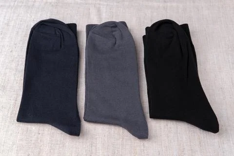 Three men's socks lie side by side on a light-colored fabric. Stock Photos