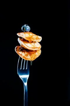 Three mini pancakes on fork, poured with honey, and blueberry on top Stock Photos