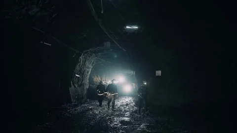 Three mining workers, in helmets, go underground through a dark tunnel. Stock Footage 240631451