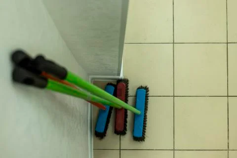 Three mops of different colors stand near the wall Stock-Fotos