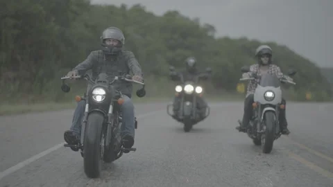 Three motorcyclists with helmets cruise down the road in the rain Stock Footage 323478935