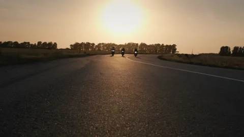 Three motorcyclists ride on an asphalt road at sunset, sun rays gleam on th.. Stock Footage 334605477