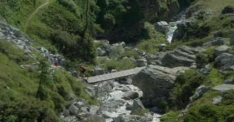 Three mountain bikers crossing a fast river over a mountain bridge. Vídeo Stock 78030839