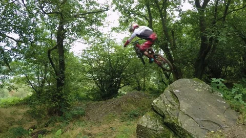 Three mountain bikers cycling off large rock jump in wood, drone aerial 4K Stock Footage 101107140