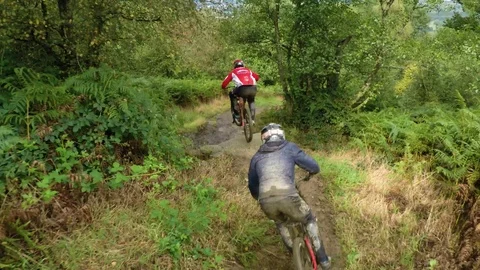 Three mountain bikers cycling through muddy wet winding trail, drone aerial 4K Stock Footage 101107332