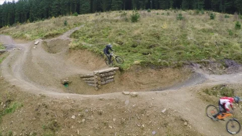 Three mountain bikers go over large man-made jump, drone aerial 4K Stock Footage 101109951