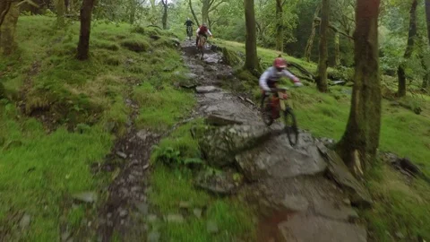 Three mountain bikers going down wet rock table wide shot , drone aerial 4K Stock Footage 101106875
