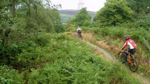 Three mountain bikers going over large jump in grassland area, drone aerial 4K Stock Footage 101107018