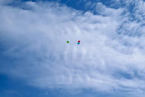 Three multi-colored balloons fly in the blue sky with clouds Stock Photos