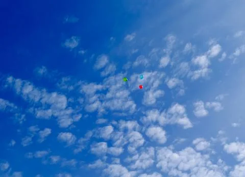 Three multi-colored balloons fly in the blue sky with clouds Stock Photos