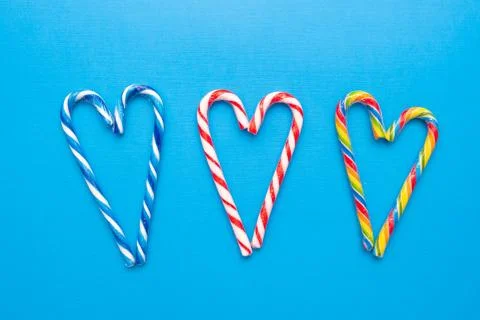 Three multi-colored candy canes in the form of a heart on a blue background Stock Photos