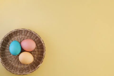 Three multi-colored easter eggs in a wicker basket on a yellow background with a Stock Photos