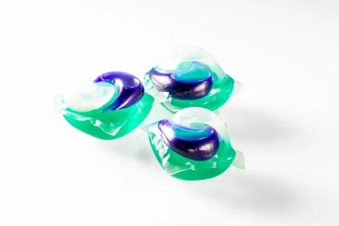 Three multi-colored gel capsules for washing clothes on a white mirror back.. Stock Photos