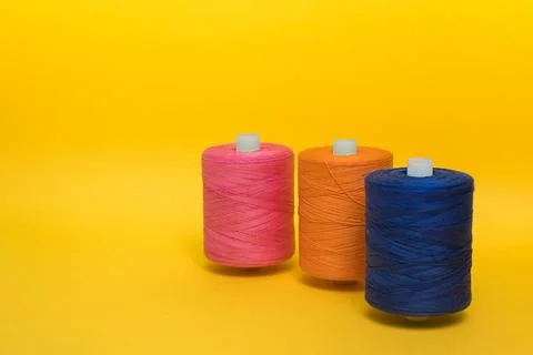 Three multi-colored large spools of thread stand one after another on a yel.. Stock Photos