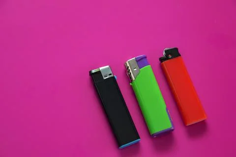 Three multi-colored lighters on a purple background. Gas lighters in black Stock Photos
