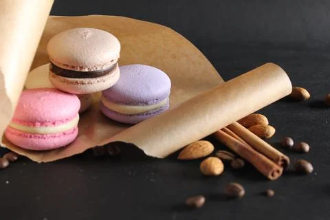 Three multi-colored macaroons lie on crafted brown paper next to lie almond s Stock Photos