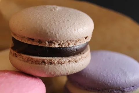 Three multi-colored macaroons lie on crafted brown paper next to lie almond s Stock Photos