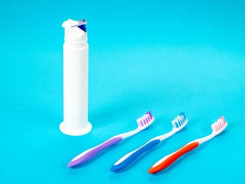 Three multi-colored toothbrushes and a tube of toothpaste on a blue backgroun Stock Photos