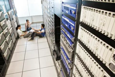Three multi-ethnic technicians working in a large computer server room. Stock Photos
