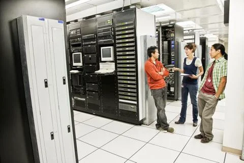 Three multi-ethnic technicians working in a large computer server room. Stock Photos