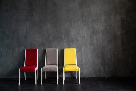 Three multicolored chairs in the interior of an empty gray room Stock Photos