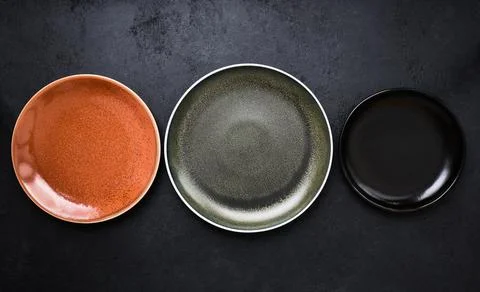 Three multicolored empty plates on black background in close-up Stock Photos