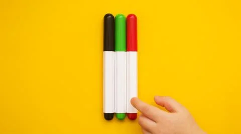 Three multicolored markers on the table. The child's hand takes the marker Stock Photos