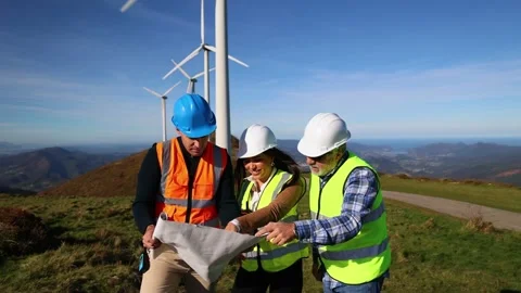 Three multiethnic engineers studying blueprint next to wind turbines Stock Footage 294975824