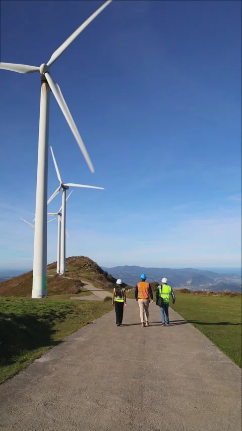 Three multiethnic engineers walking on road discussing about wind turbine Stock Footage 294976144