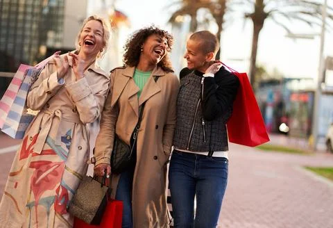 Three multiethnic girlfriends having fun, shopping and laughing while walking on Stock Photos