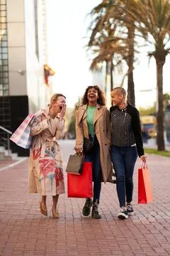 Three multiethnic girlfriends having fun, shopping and laughing while walking on Stock Photos
