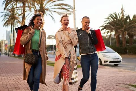 Three multiethnic girlfriends having fun, shopping and laughing while walking on Stock Photos
