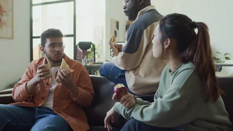 Three Multiethnic Programmers Talking while Having Lunch on Couch in Office Video stock 293173765