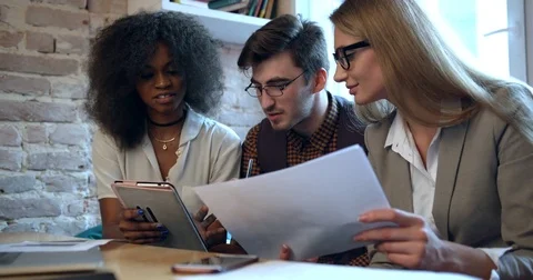 Three multirace colleagues are having fun while talking and using the tablet at Stock Footage 84041070
