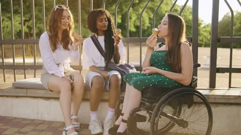 Three multiracial friends enjoy ice cream on a sunny day while sitting on a Stock Footage 313400018
