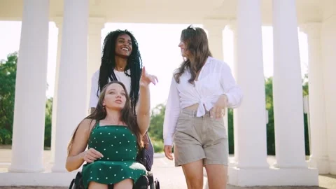Three multiracial friends one disabled in a wheelchair enjoy a sunny day while Stock Footage 313399579