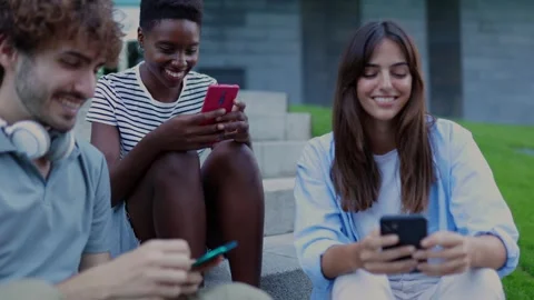 Three multiracial young friends having fun using mobile phone sitting outdoors. Stock Footage 274762512