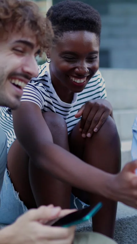 Three multiracial young friends having fun using mobile phone sitting outdoors. Stock Footage 310779652