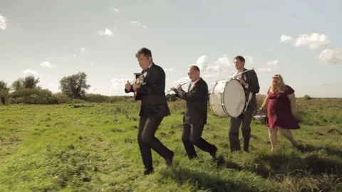 Three musicians and a merry fat girl are dancing on the field. Stock Footage