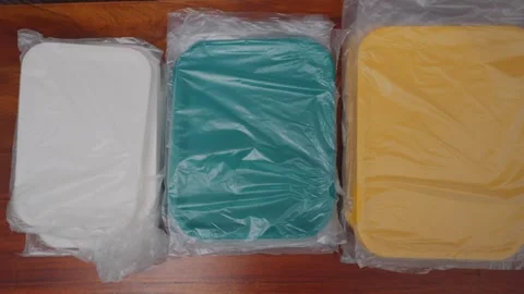 Three New Rectangular Plastic Containers in White, Teal, and Yellow on a Wooden Video stock 333321543