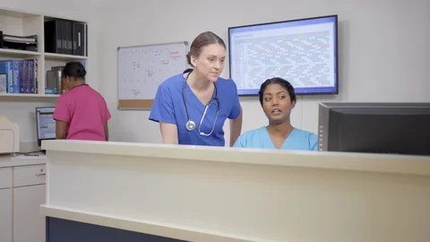 Three nurses at nursing station, two talk, camera move left right, stethoscope Stock Footage 109502255