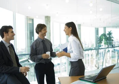 Three office workers standing with cups of coffee, talking Foto stock