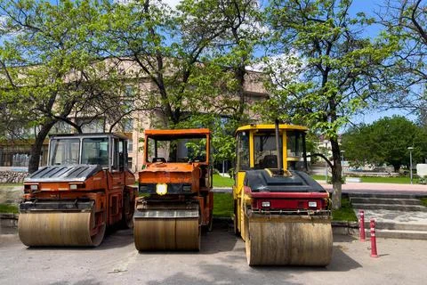 Three old asphalt rollers stand on the side of the road. Stock Photos