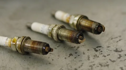 Three old dirty spark plugs with brown oil stains on a metal surface Stock Footage 336711904