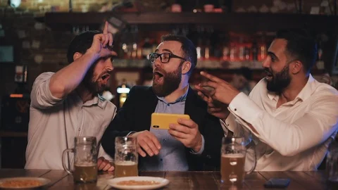 Three old friends watching video on smartphone and drinking draft beer in the Stock Footage 109596258