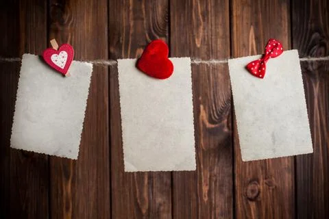 Three old paper sheet with bow and hearts hanging on clothesline against wood Foto stock