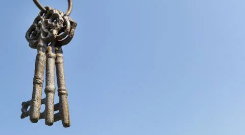 Three old rusty keys hang in the foreground against a blue sky Stock Photos
